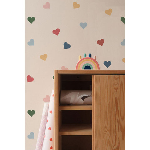 2. Close-up of colorful heart-patterned wallpaper by Dekornik behind a wooden cabinet with a rainbow toy on top