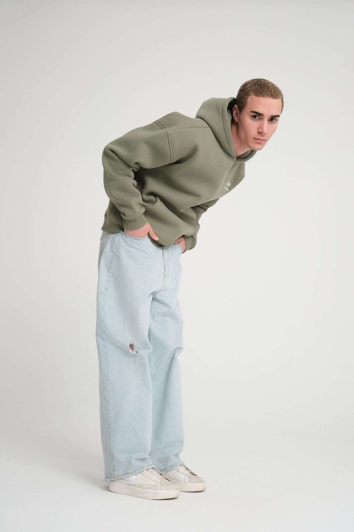1. Full body view of man wearing olive green hoodie and light jeans, posing in studio
