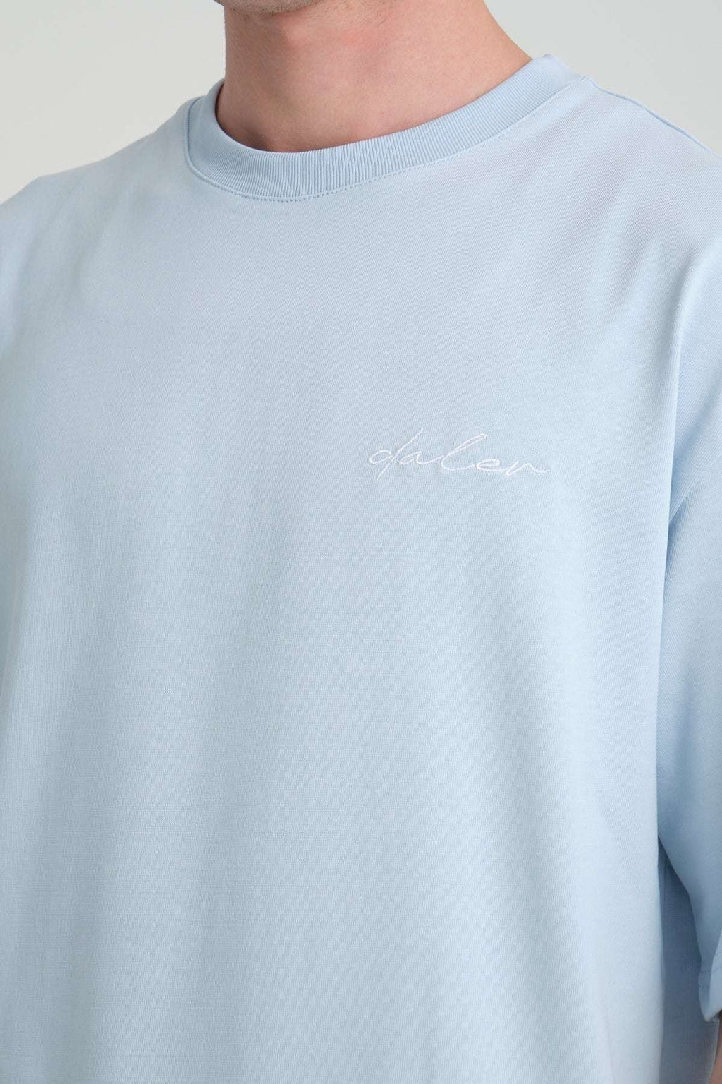 3. Close-up of DalerClo logo embroidery on baby blue heavyweight t-shirt, showcasing fabric texture and color