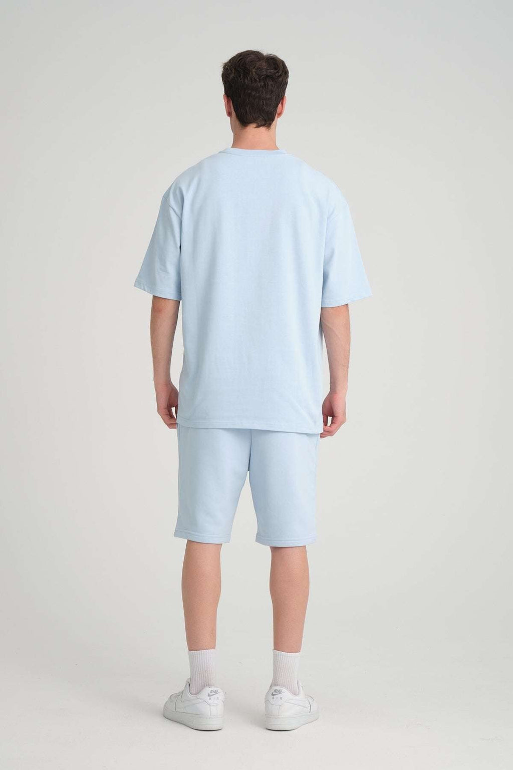 1. Man wearing baby blue oversized t-shirt and shorts, shown from back, in studio setting