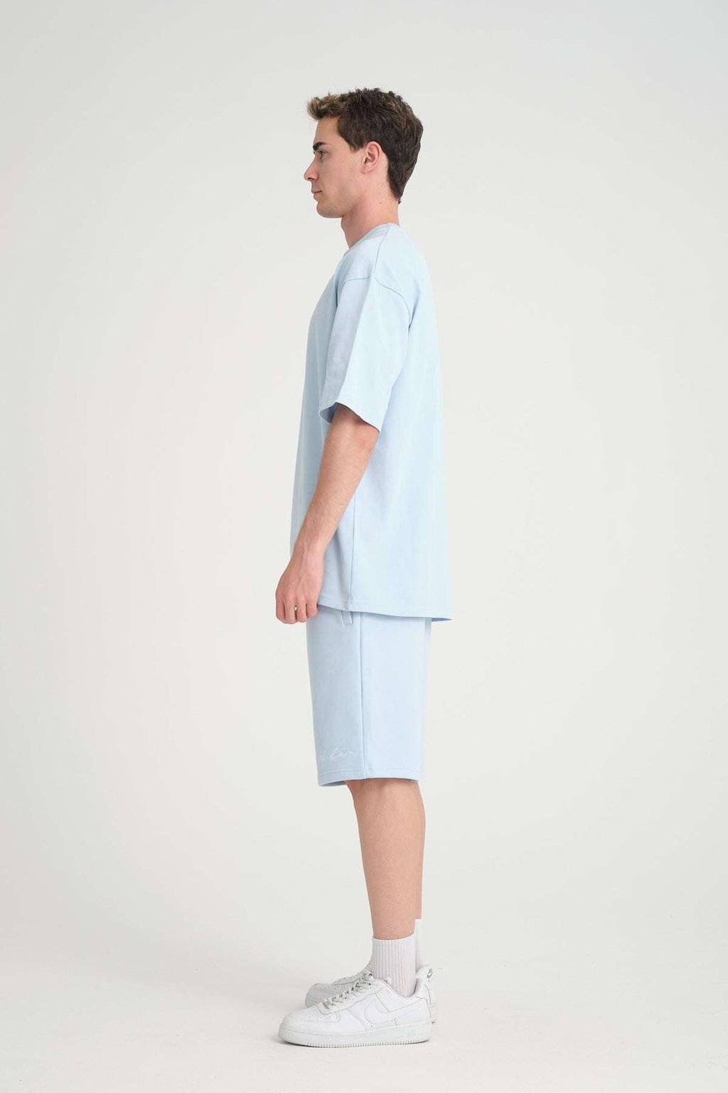 1. Man in baby blue oversized t-shirt and shorts, side view, in studio setting