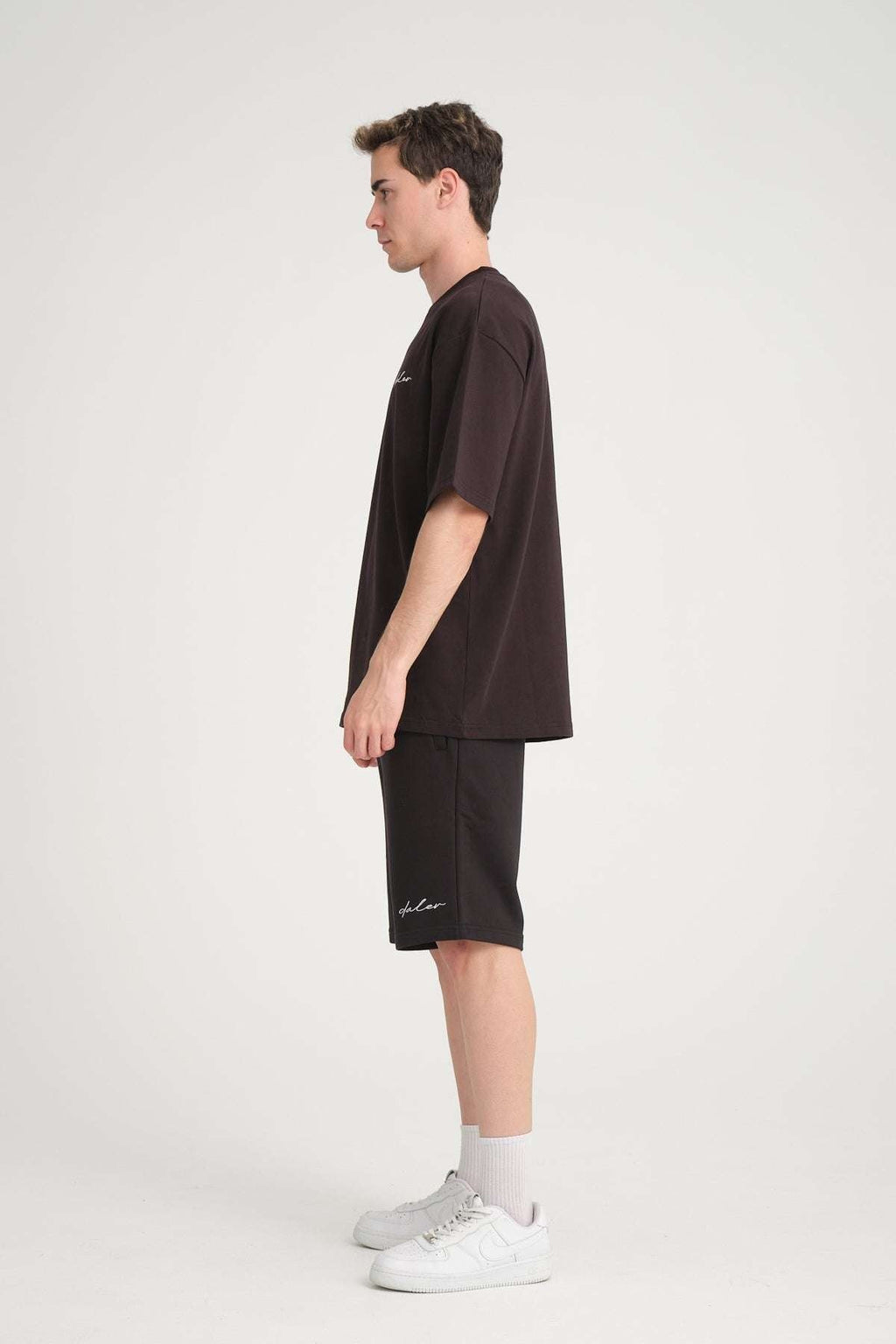 4. Side view of man wearing black oversized DalerClo t-shirt and shorts with white sneakers