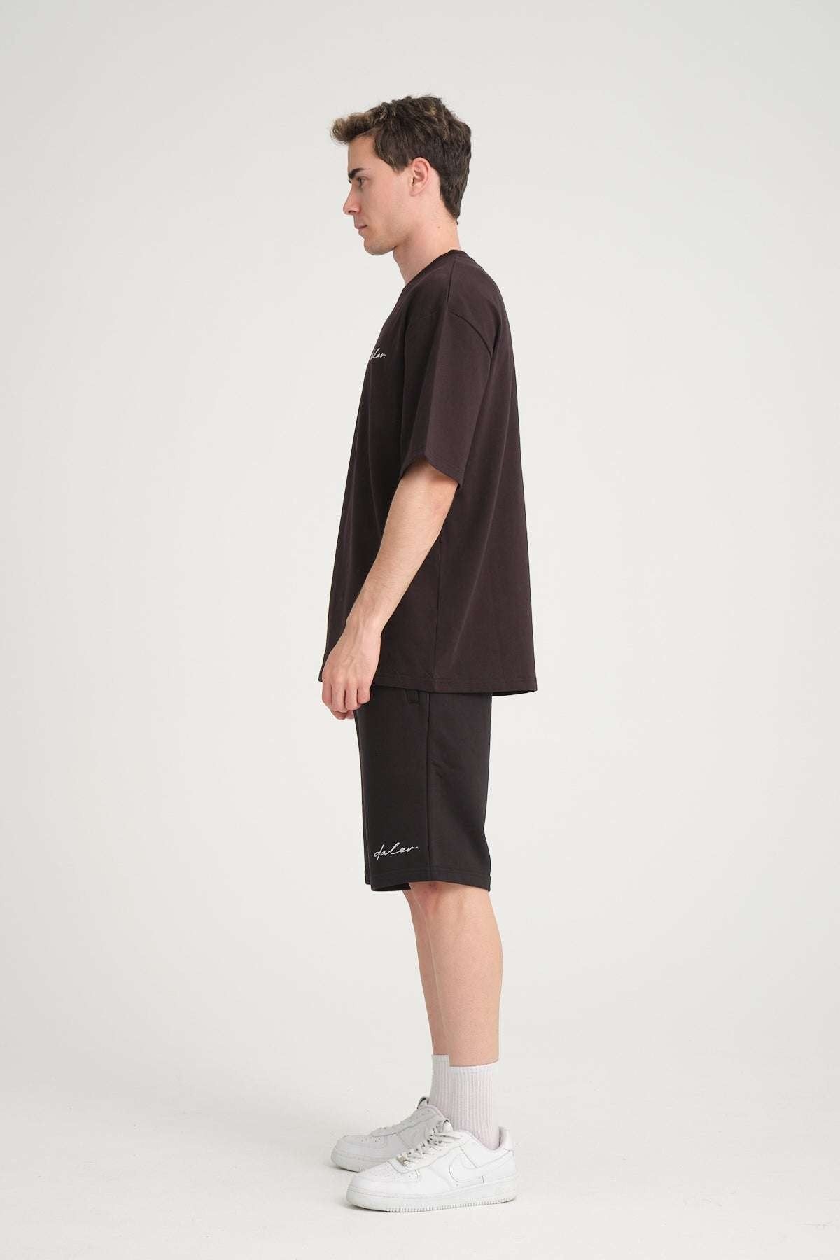 4. Side view of man wearing black oversized DalerClo t-shirt and shorts with white sneakers
