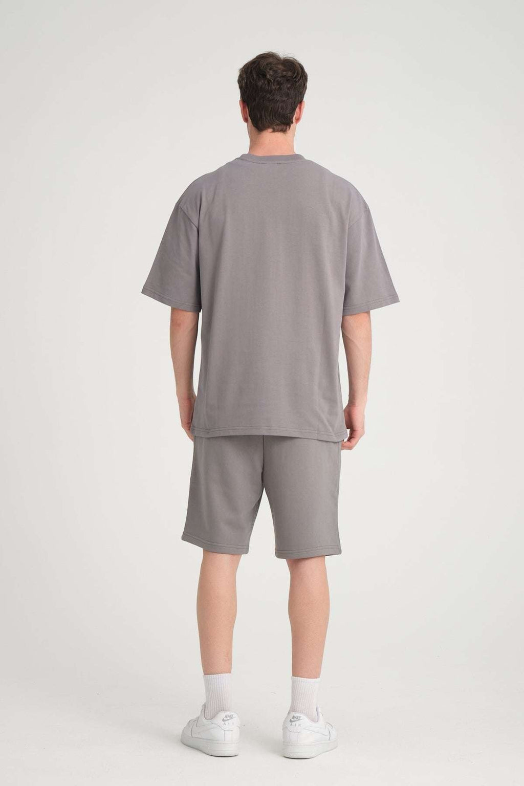2. Back view of man wearing grey oversized t-shirt and shorts in studio setting