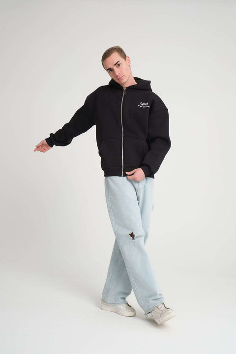 2. Man wearing black DalerClo hoodie with front zipper and logo, paired with light blue jeans, standing in a relaxed pose.