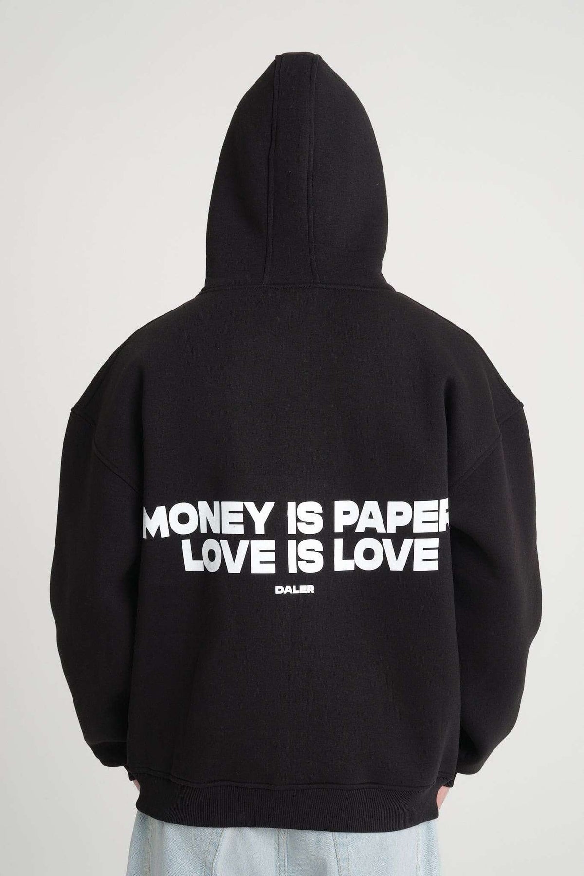 1. Back view of black hoodie with bold white text 'Money is Paper, Love is Love' worn by a person, showcasing oversized fit and hood.