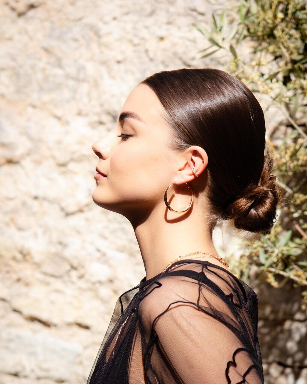 1. Woman wearing MyaMoon Helena Hoops Earrings in rose gold and silver, styled with a black sheer top, outdoors