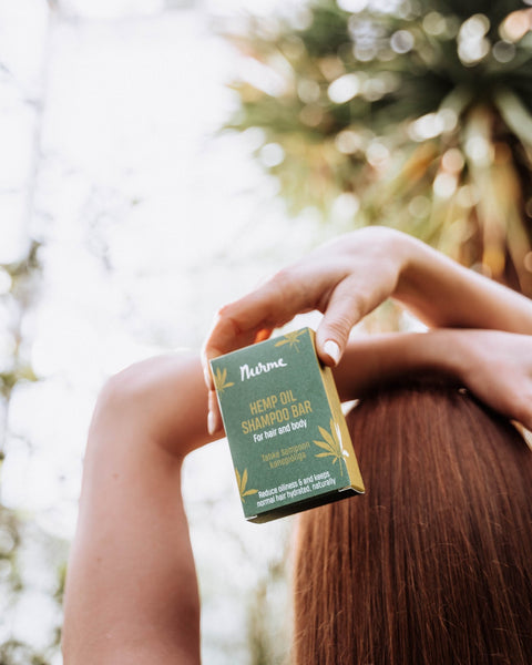 1. Woman holding Nurme Hemp Oil Shampoo Bar with green packaging in outdoor setting, showcasing long brown hair