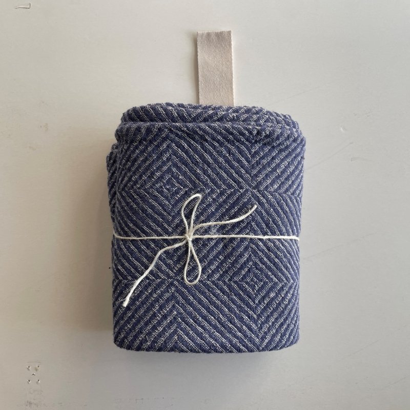 1. Rolled blue fishbone pattern linen towel with white cotton hanger and tied with string on a plain background