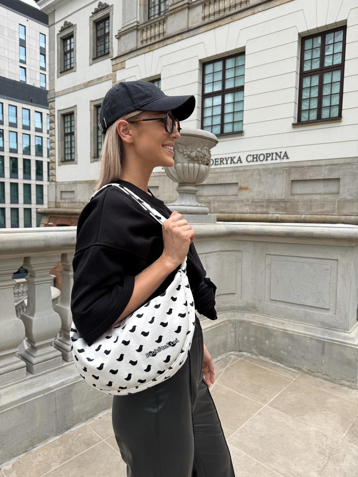 1. Woman wearing Garbanota Hobo Bag Birds in white with black bird pattern, styled casually outdoors