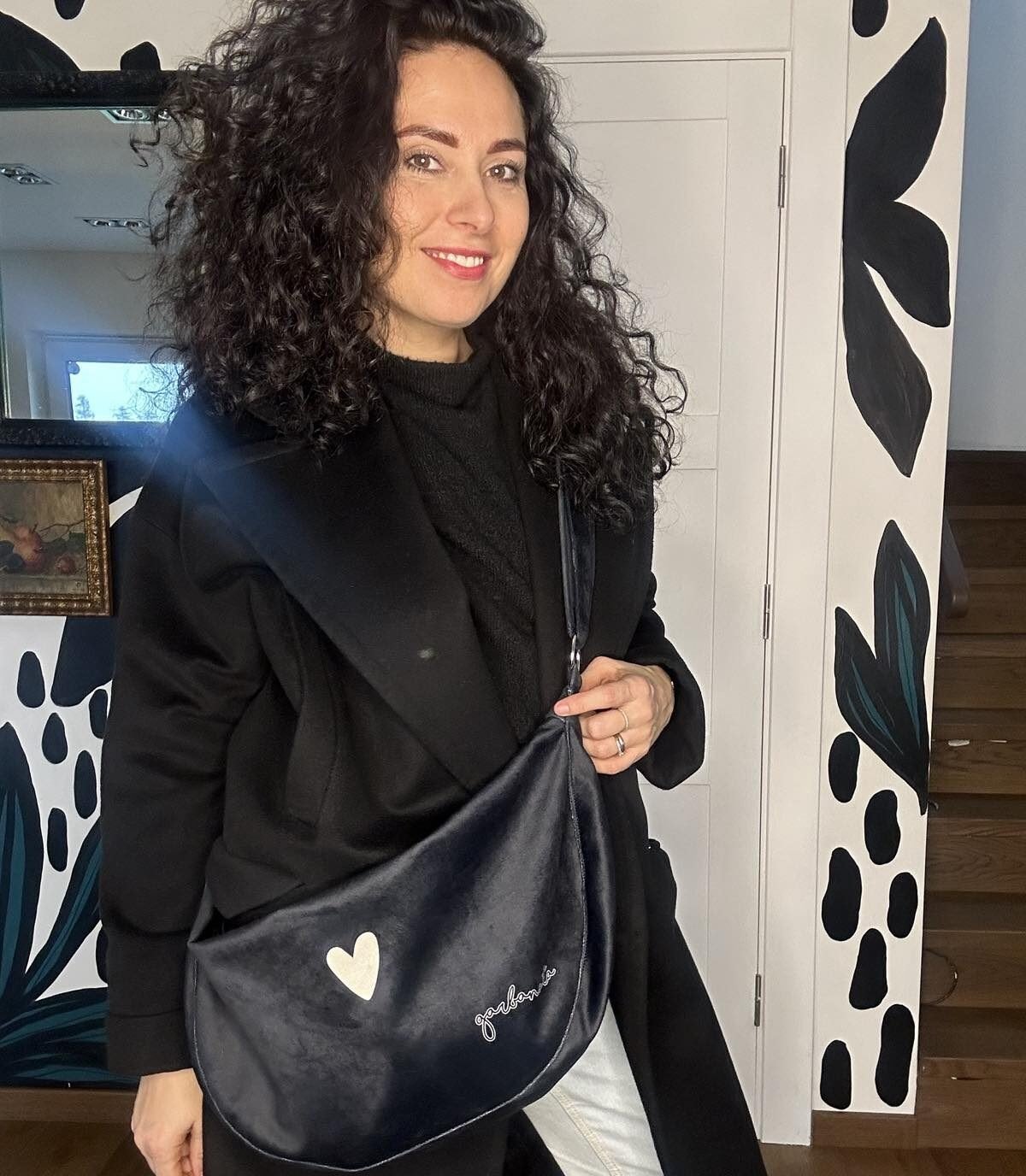 1. Woman wearing Garbanota Hobo Bag Heart in black with heart detail, styled with black outfit outdoors