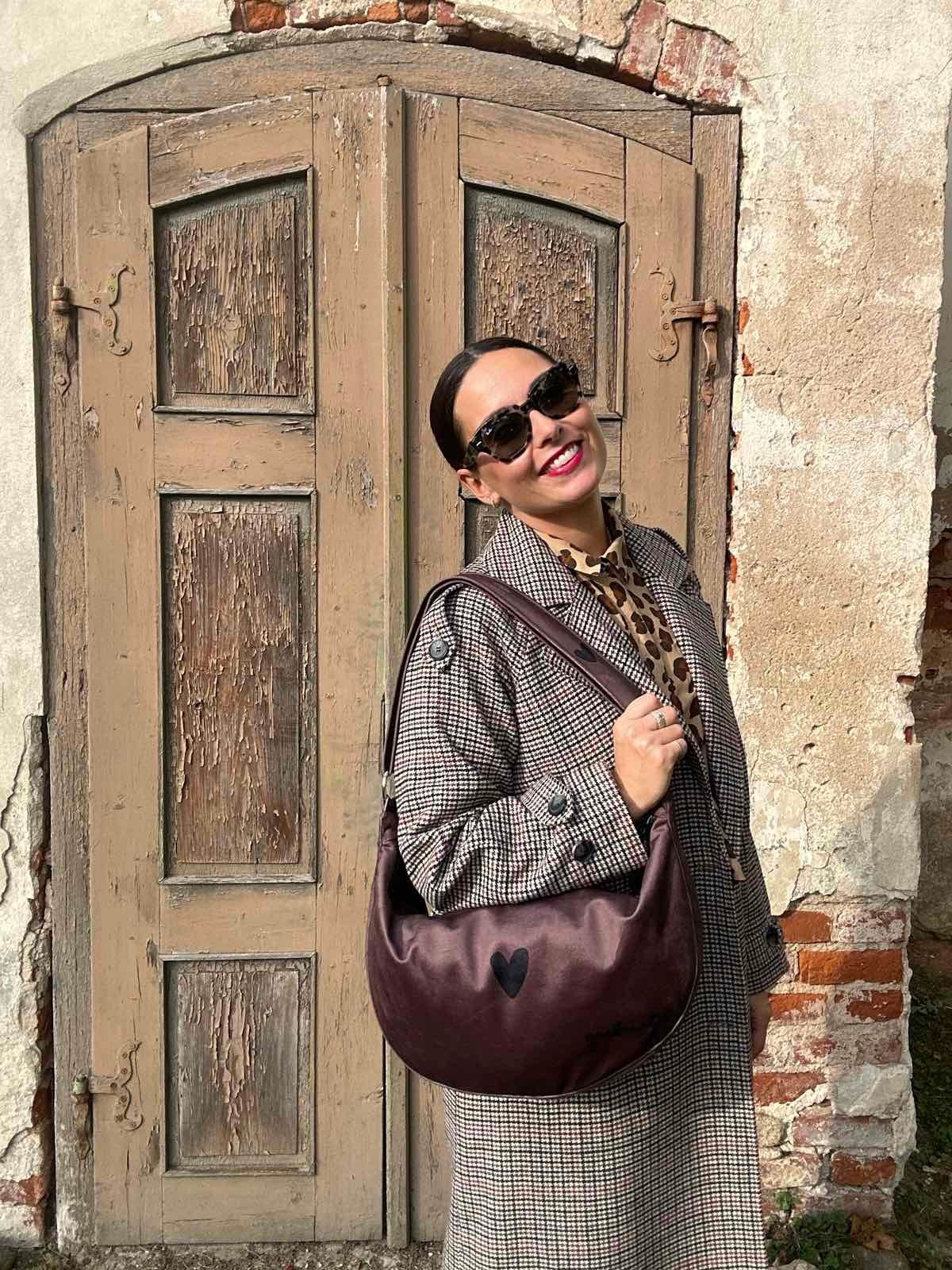 1. Woman wearing Garbanota Hobo Bag Heart in brown velour, standing outdoors with vintage door backdrop