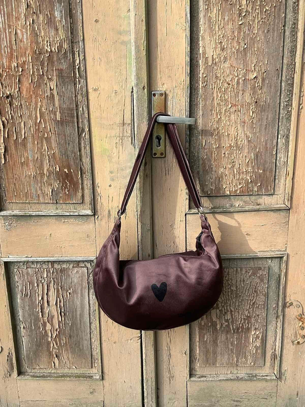 3. Garbanota Hobo Bag Heart in brown velour hanging on rustic door, showcasing heart detail
