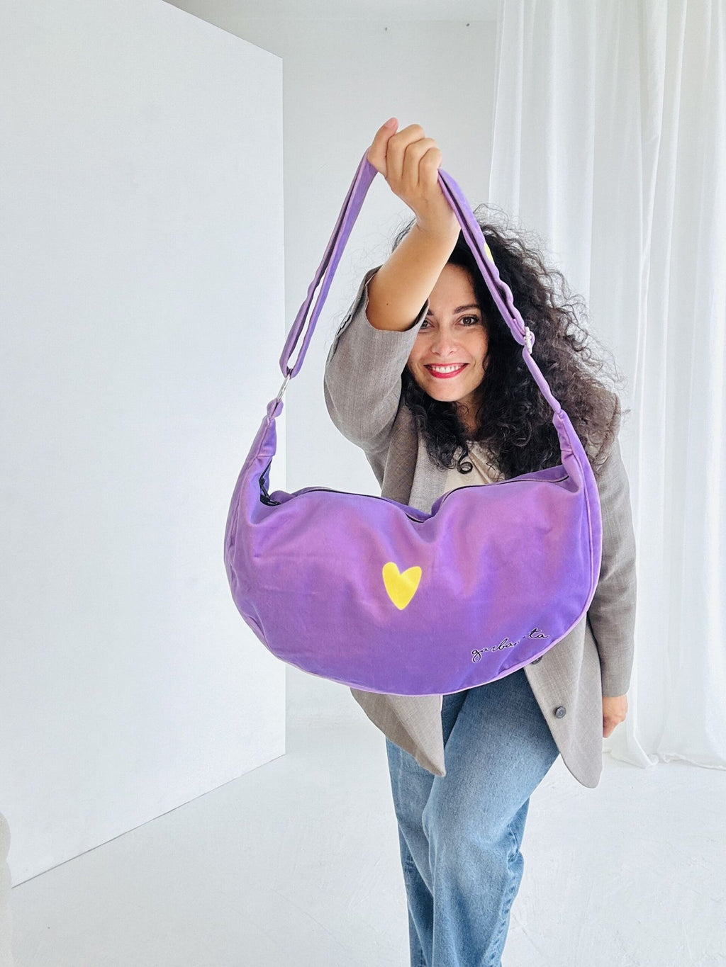 1. Woman holding Garbanota Hobo Bag Heart in purple with yellow heart detail, showcasing adjustable strap in lifestyle setting