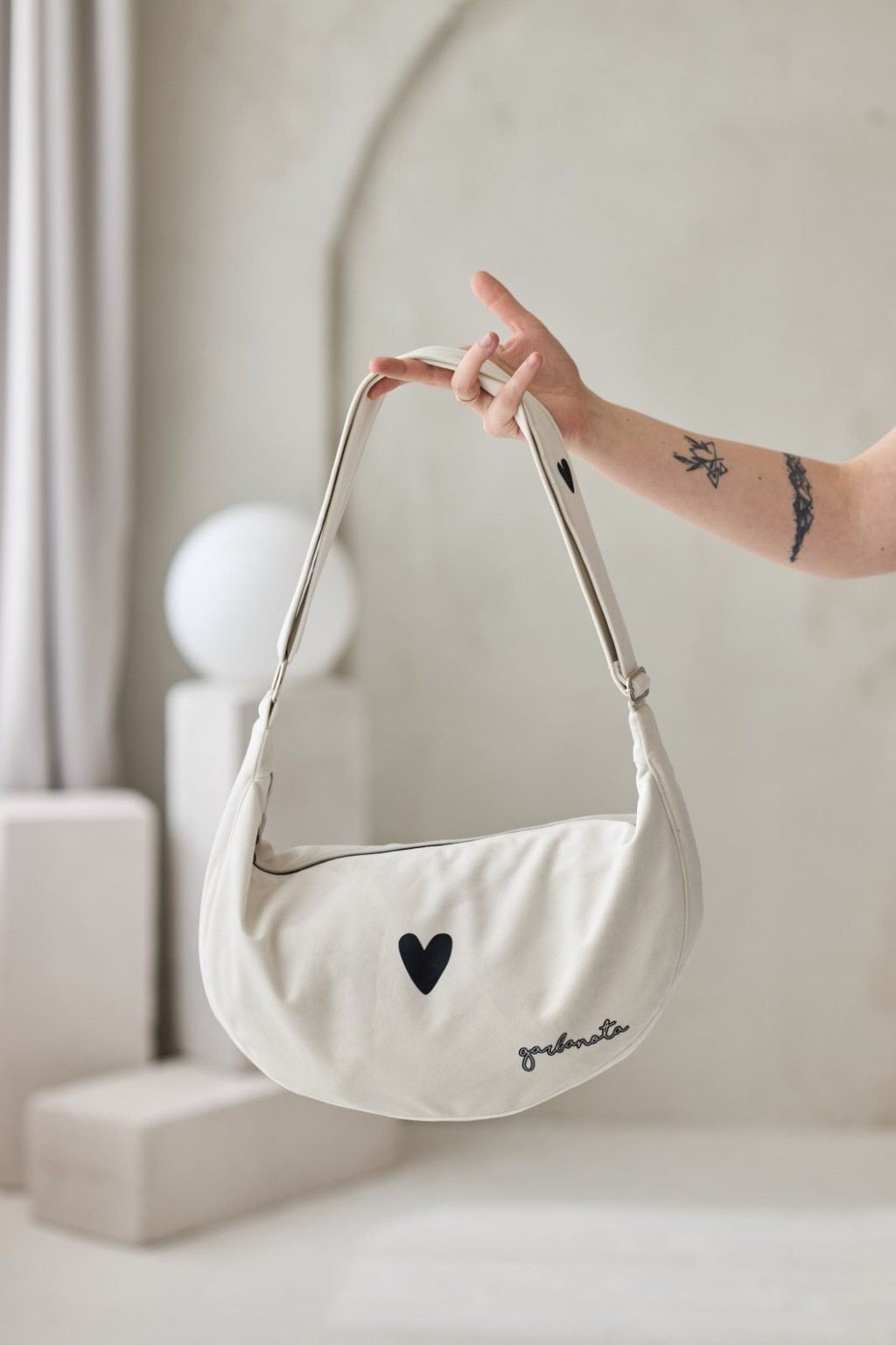 1. Garbanota Hobo Bag Heart in white held by a person, showcasing heart detail and adjustable strap in studio setting