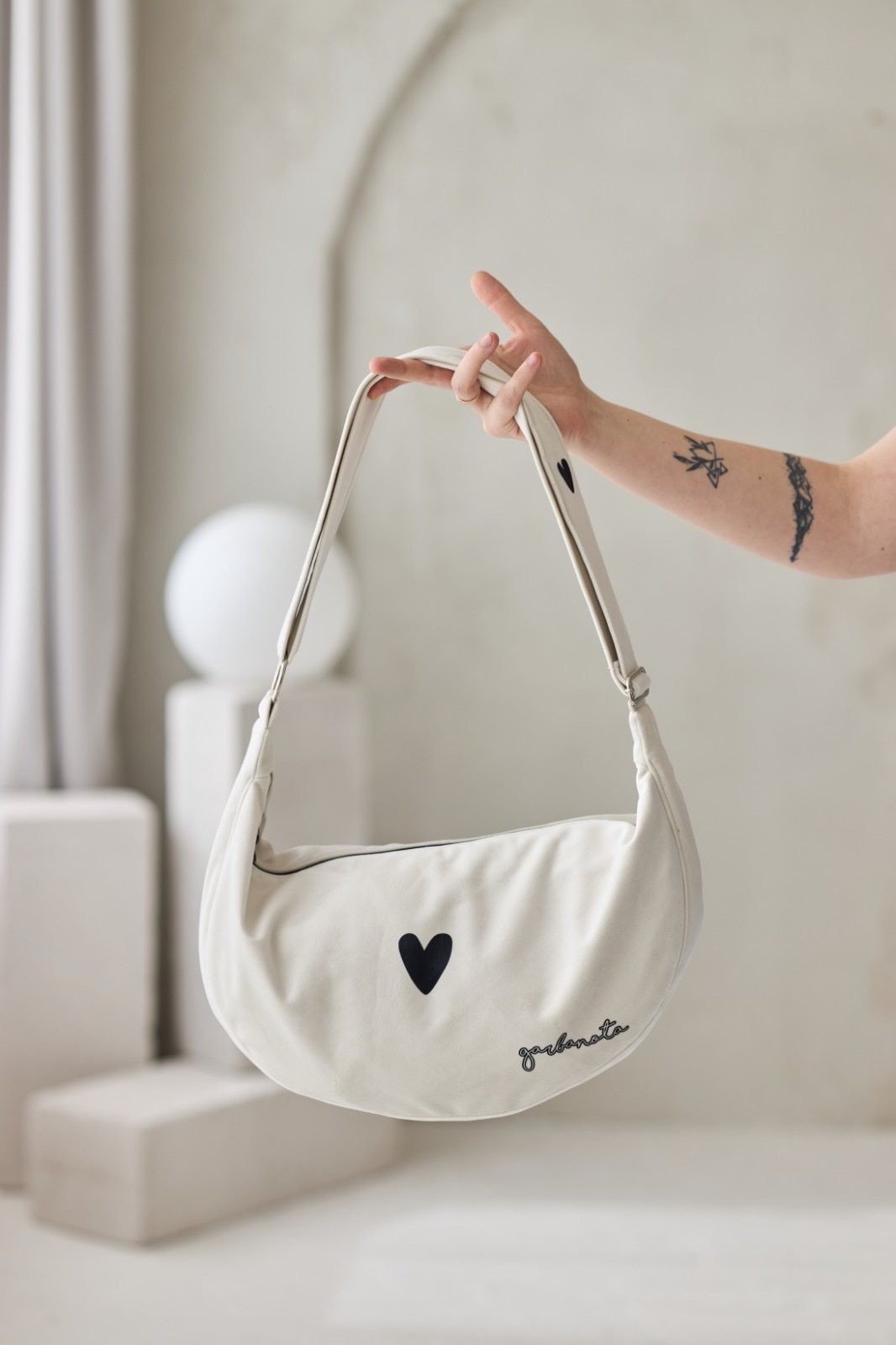 1. Garbanota Hobo Bag Heart in white held by a person, showcasing heart detail and adjustable strap in studio setting