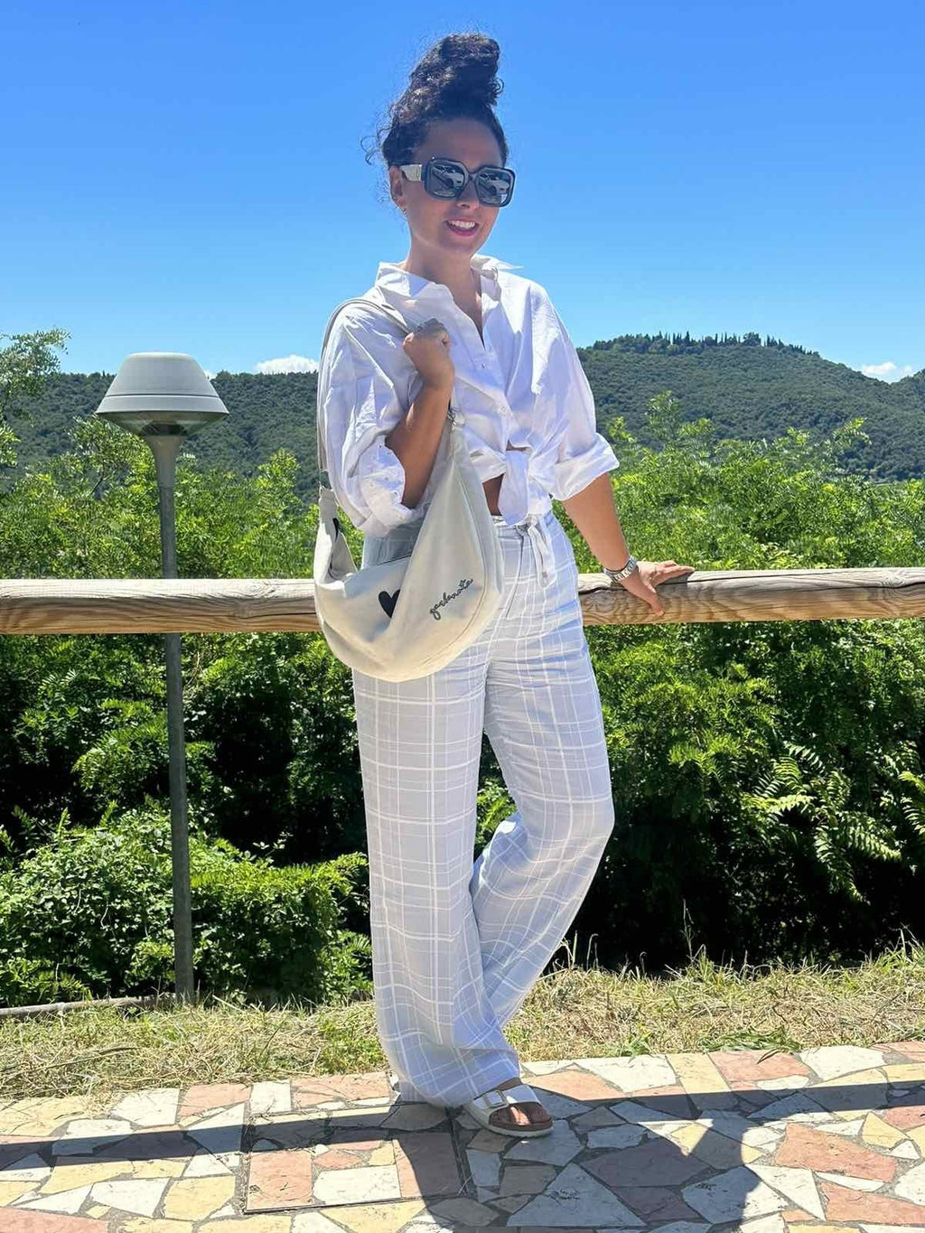 2. Woman standing on balcony with Garbanota Hobo Bag Heart in white, wearing all-white outfit