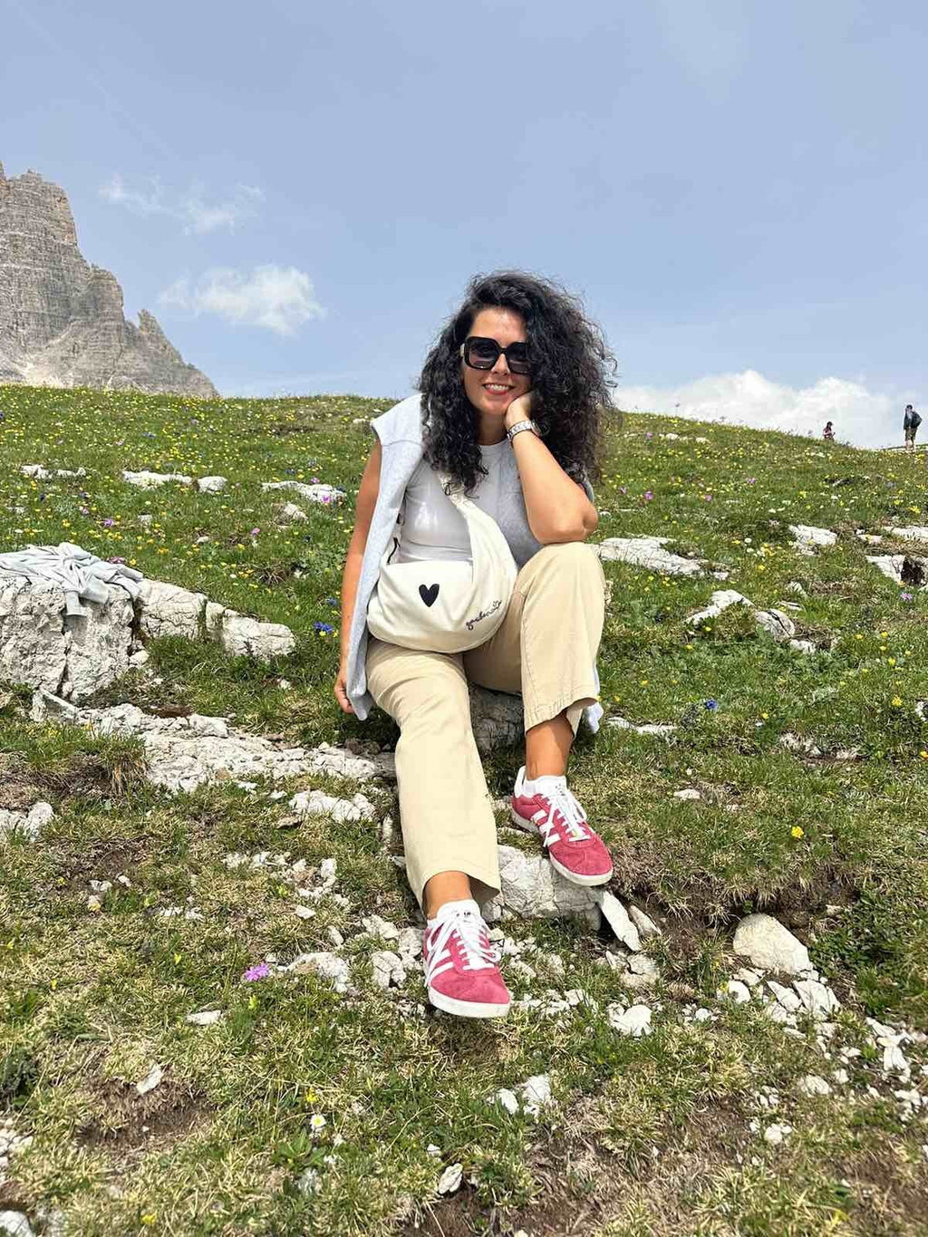 1. Woman sitting on grass with Garbanota Hobo Bag Heart in white, showcasing casual outdoor style