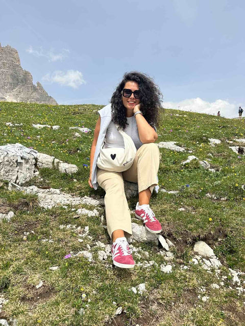1. Woman sitting on grass with Garbanota Hobo Bag Heart in white, showcasing casual outdoor style