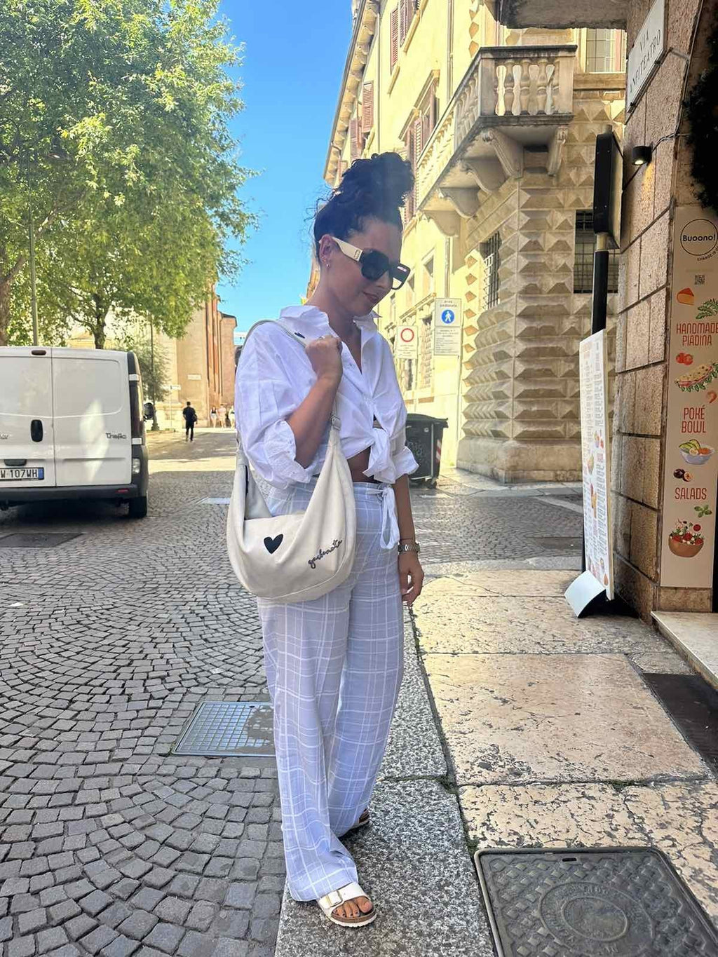 10. Woman in city square with Garbanota Hobo Bag Heart in white, wearing sunglasses and white ensemble
