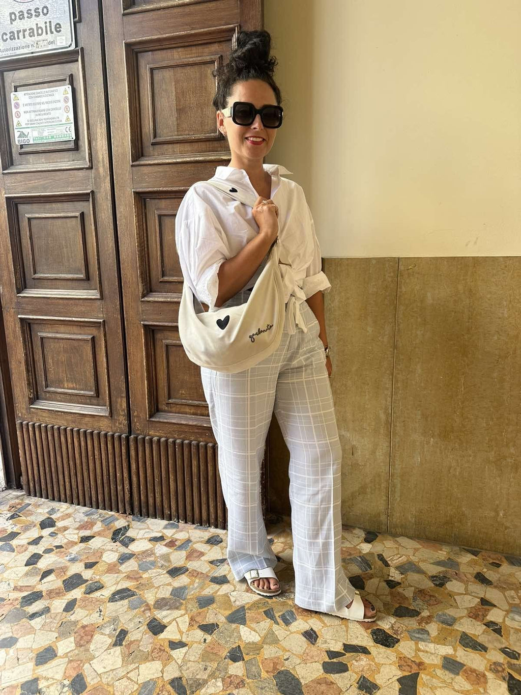 9. Woman standing in urban setting with Garbanota Hobo Bag Heart in white, wearing white outfit