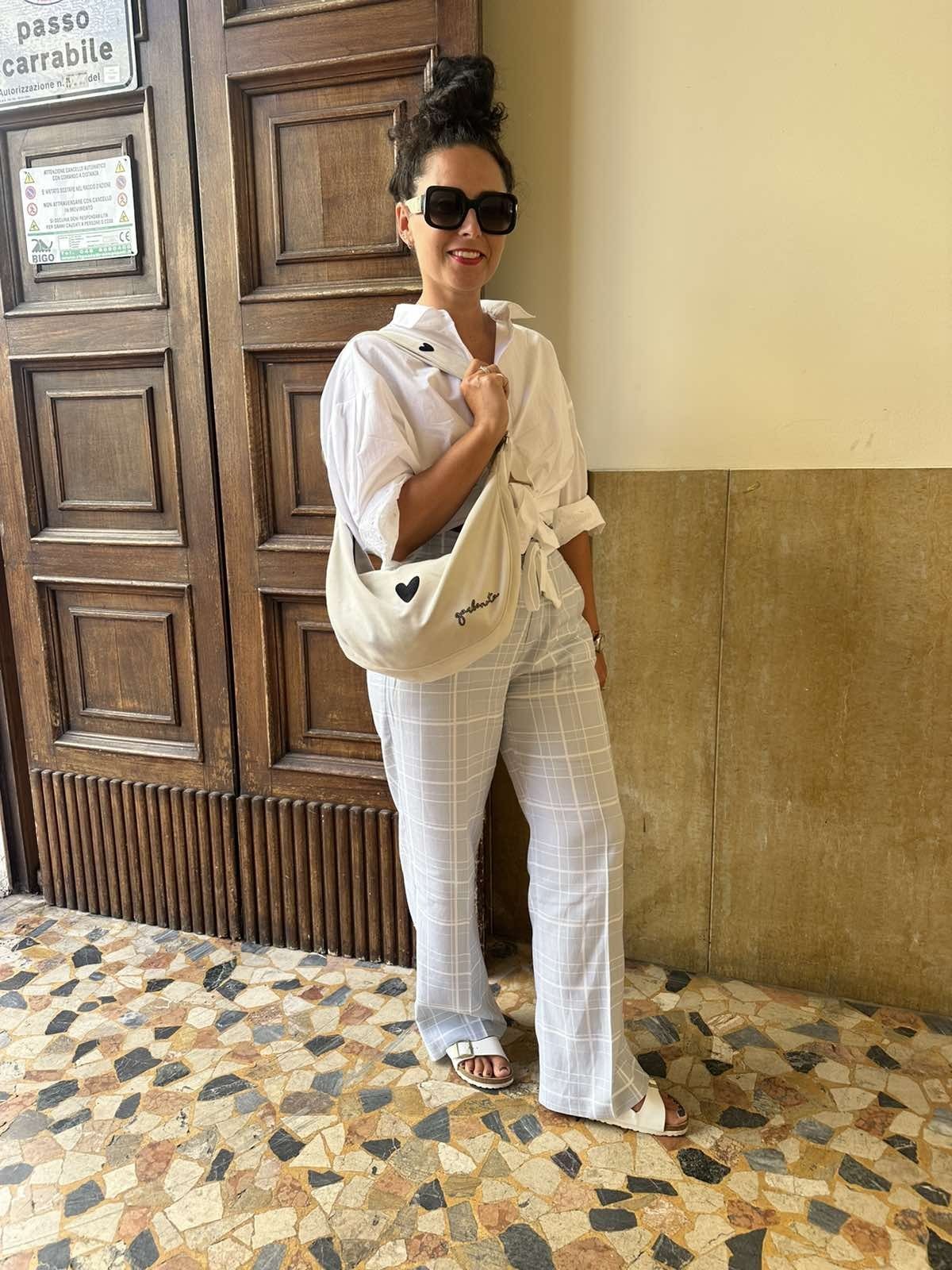 9. Woman standing in urban setting with Garbanota Hobo Bag Heart in white, wearing white outfit