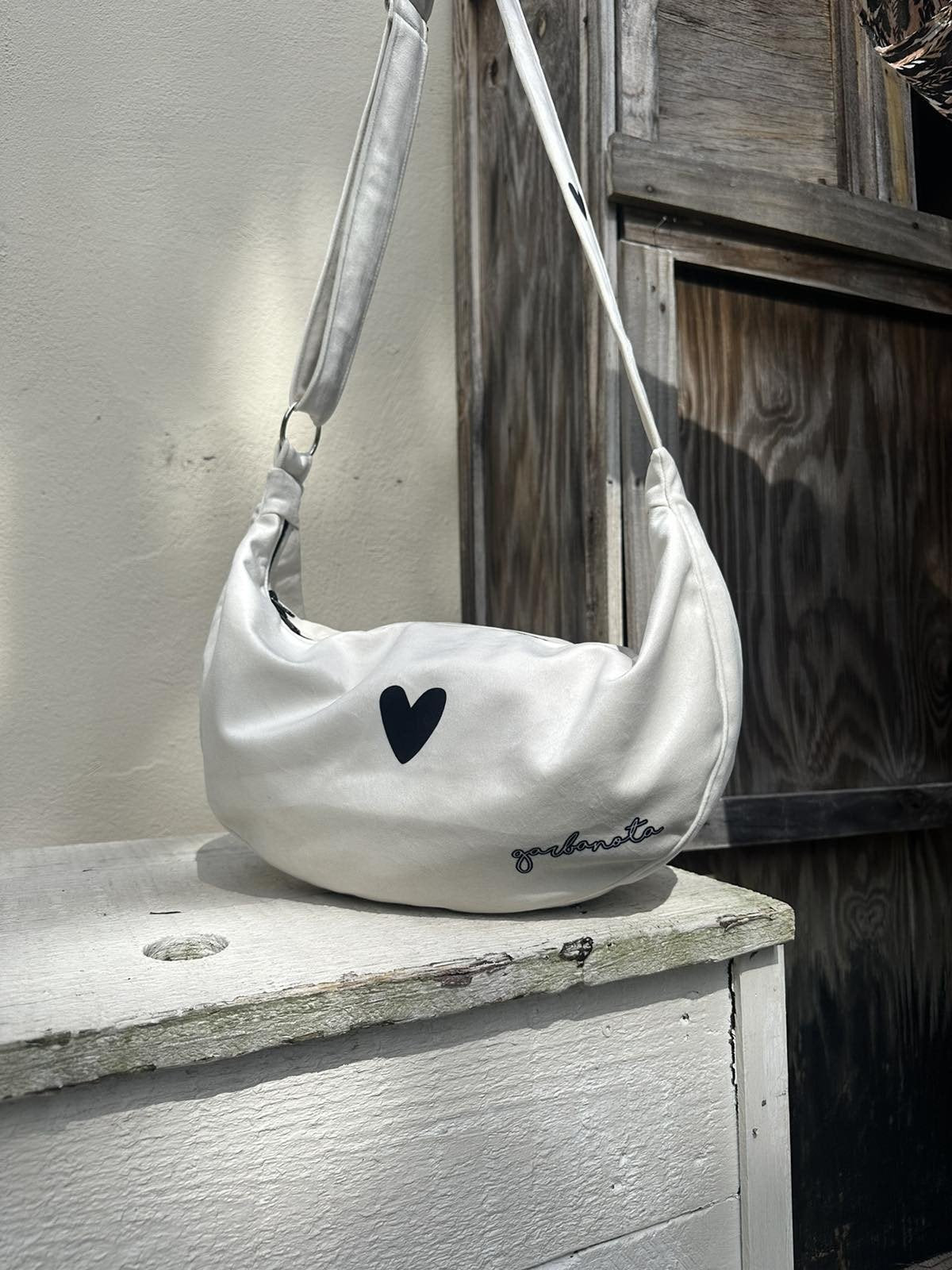 13. Garbanota Hobo Bag Heart in white on rocky shore, showing heart detail and durable material