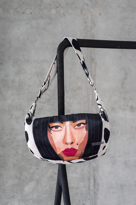 2. Garbanota KIYOKO Hobo Bag with face illustration, hanging on a black stand in a studio setting