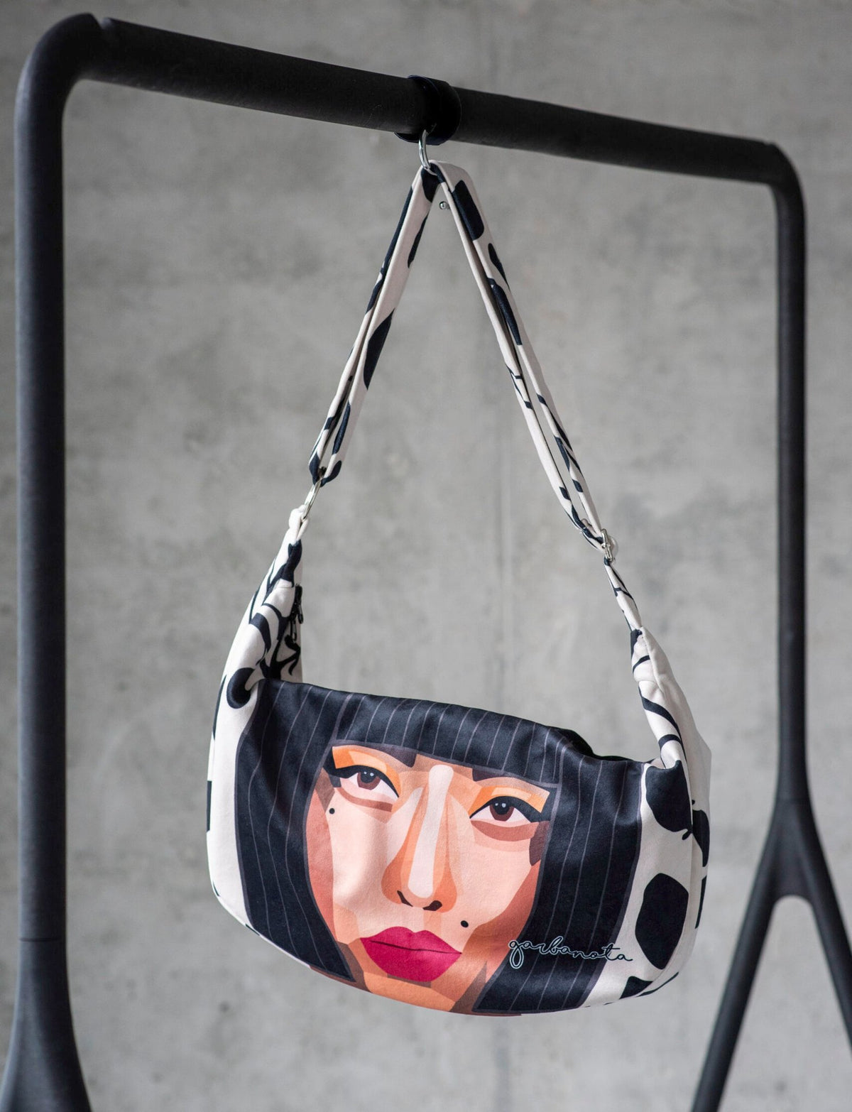 3. Garbanota KIYOKO Hobo Bag featuring a face design, displayed on a black rail in a studio