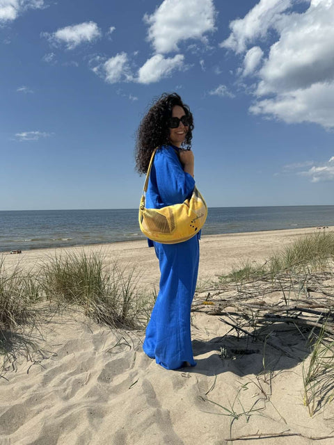 3. Woman carrying Garbanota Hobo Bag in Lemon, back view on a beach, emphasizing adjustable strap and design