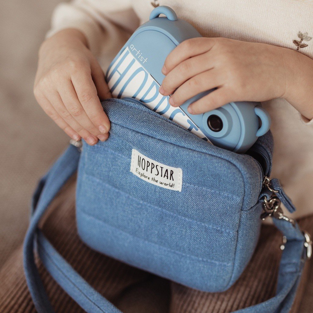 31. Person placing blue Hoppstar camera into matching bag, close-up view