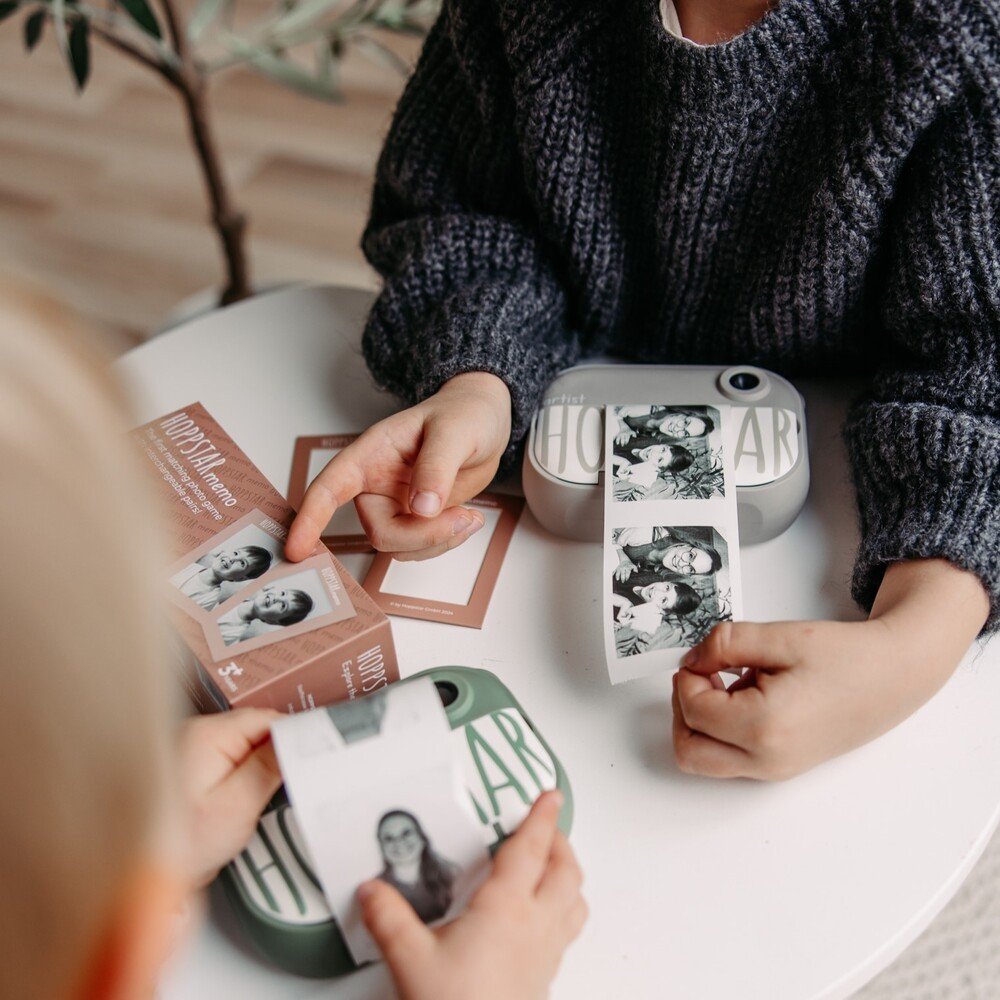 1. Two children using Hoppstar Artist camera to print photos for memory game on a white table