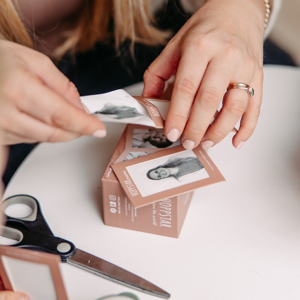 3. Close-up of hands placing photo into Hoppstar Memory Game envelope with scissors nearby