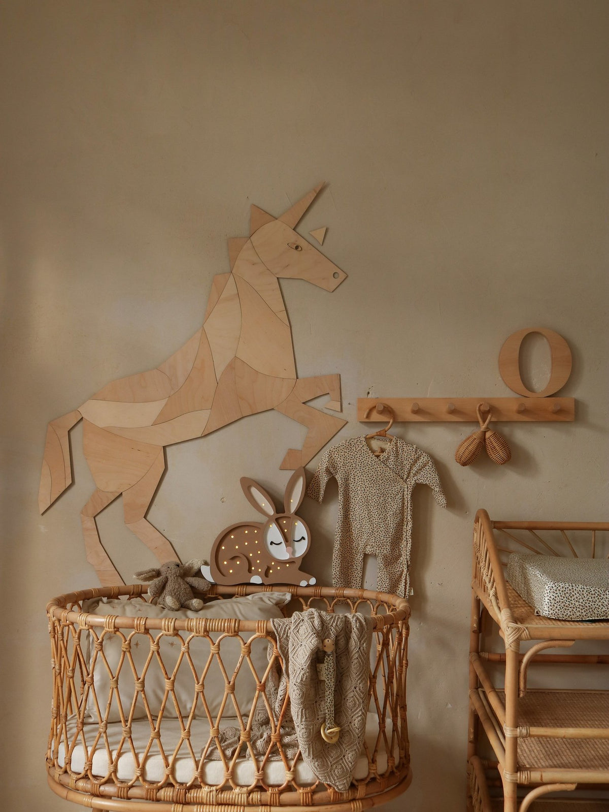 5. Wooden origami unicorn wall decoration above a rattan crib with baby clothes and toys