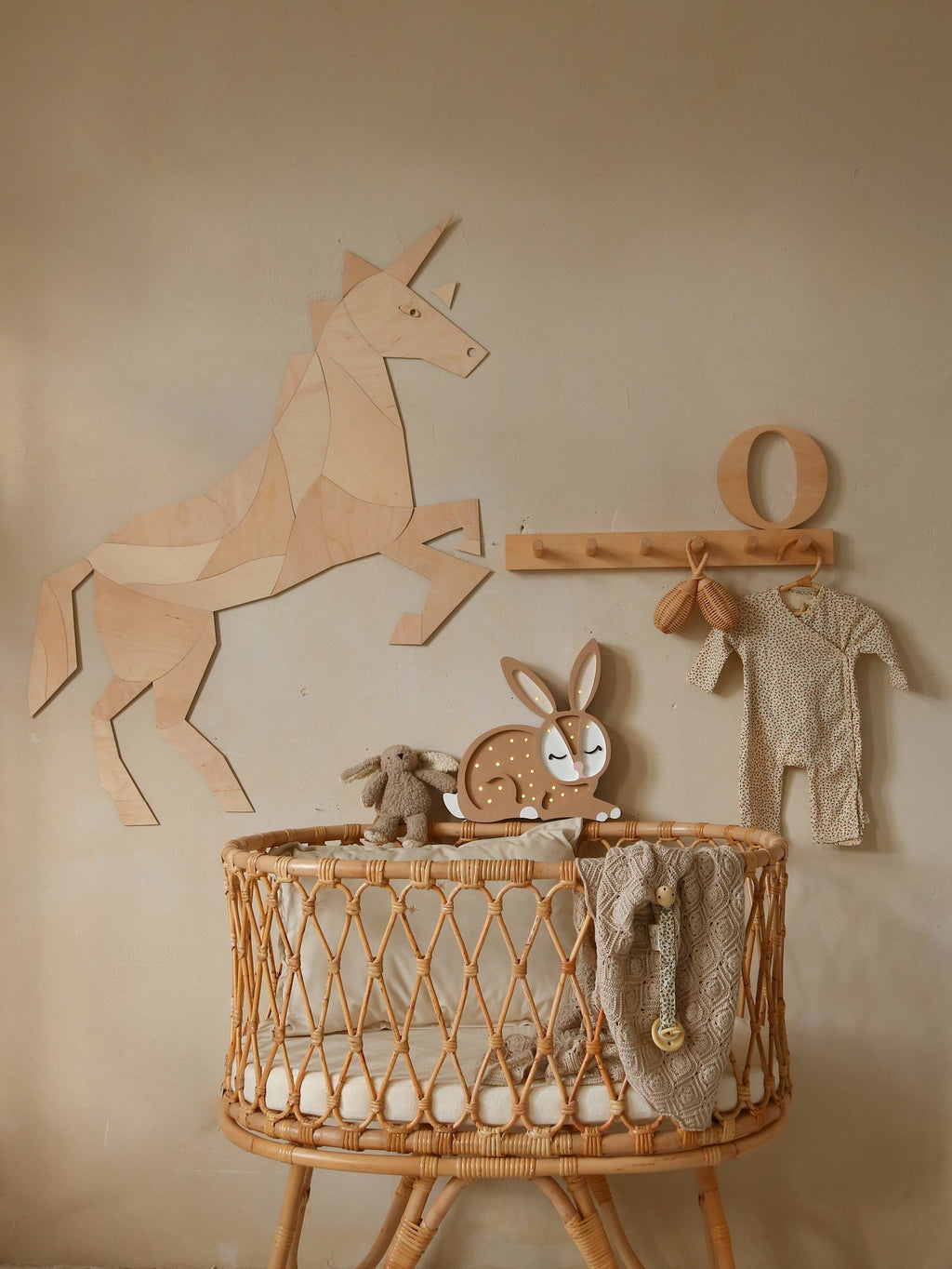 6. Wooden origami unicorn wall decoration above a rattan crib with plush toys and baby clothes