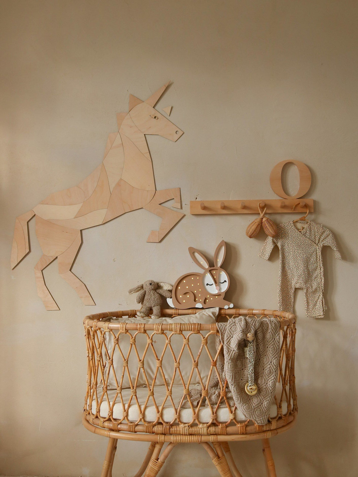6. Wooden origami unicorn wall decoration above a rattan crib with plush toys and baby clothes