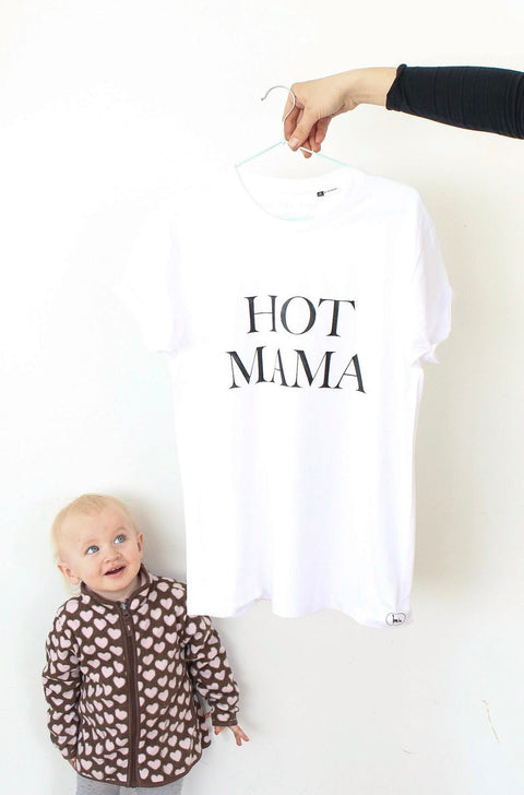 1. White Hot Mama T-shirt by Black Giraffe Brand, shown hanging with bold text, next to a child in a heart-patterned jacket