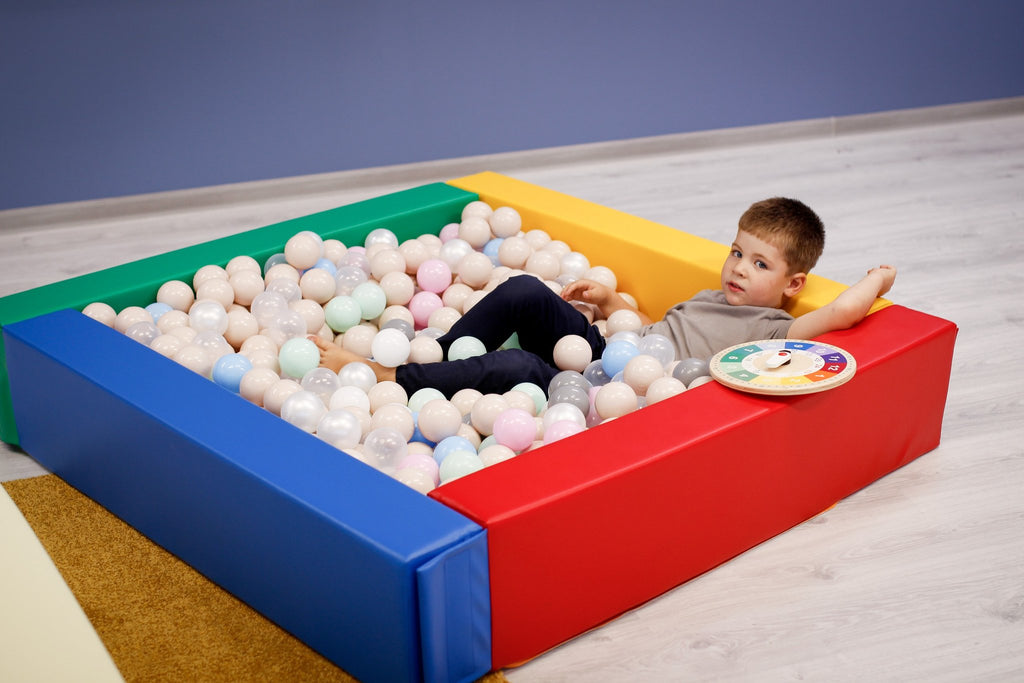 1. Child relaxing in a multicolor IGLU soft play ball pit filled with pastel balls indoors