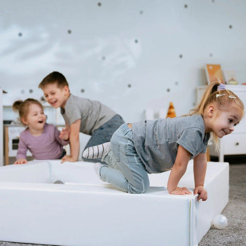 3. Three children climbing and playing on a white IGLU ball pit in a room with a dotted wall