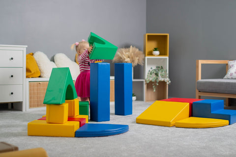 5. Girl in pink dress stacking multicolor foam blocks in a playroom
