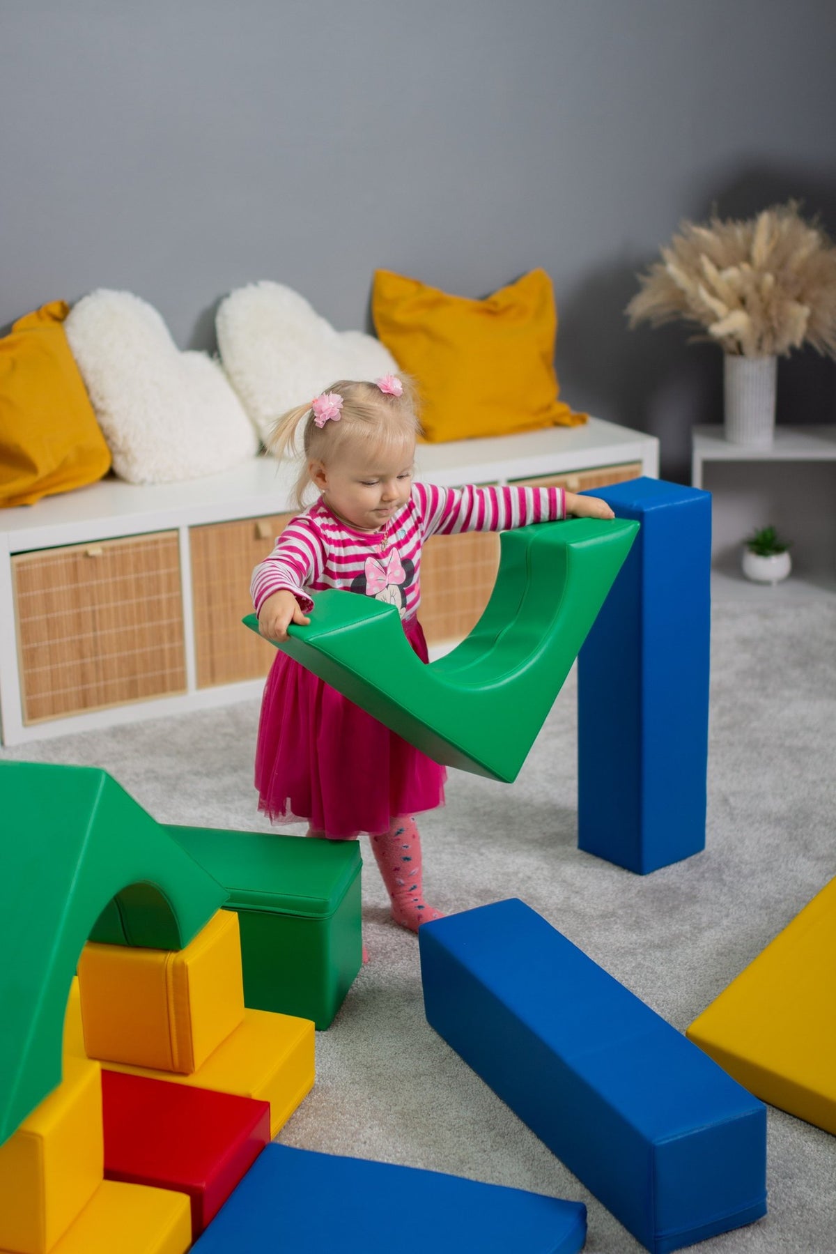 9. Girl in pink dress holding green foam block in a playroom
