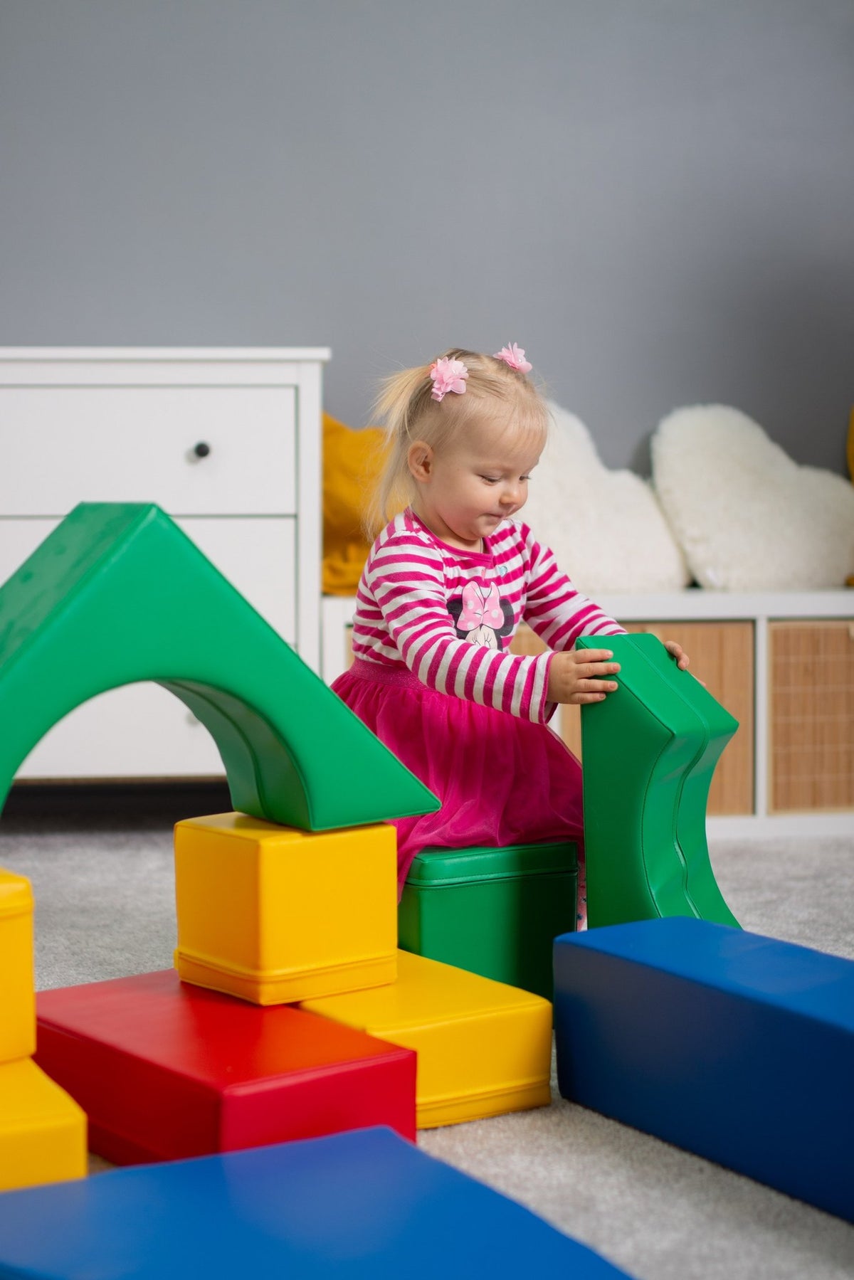 16. Girl in pink dress assembling multicolor foam blocks in a playroom