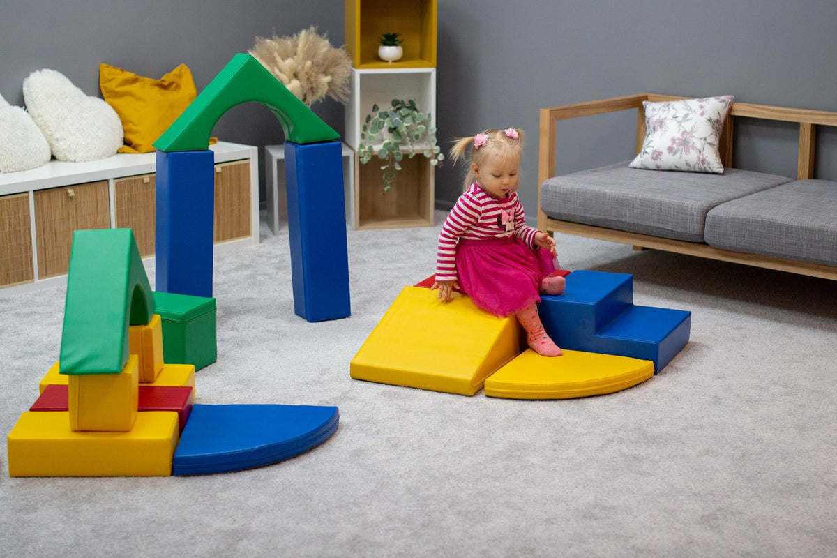 7. Girl sitting on yellow foam block steps with multicolor blocks around in a playroom