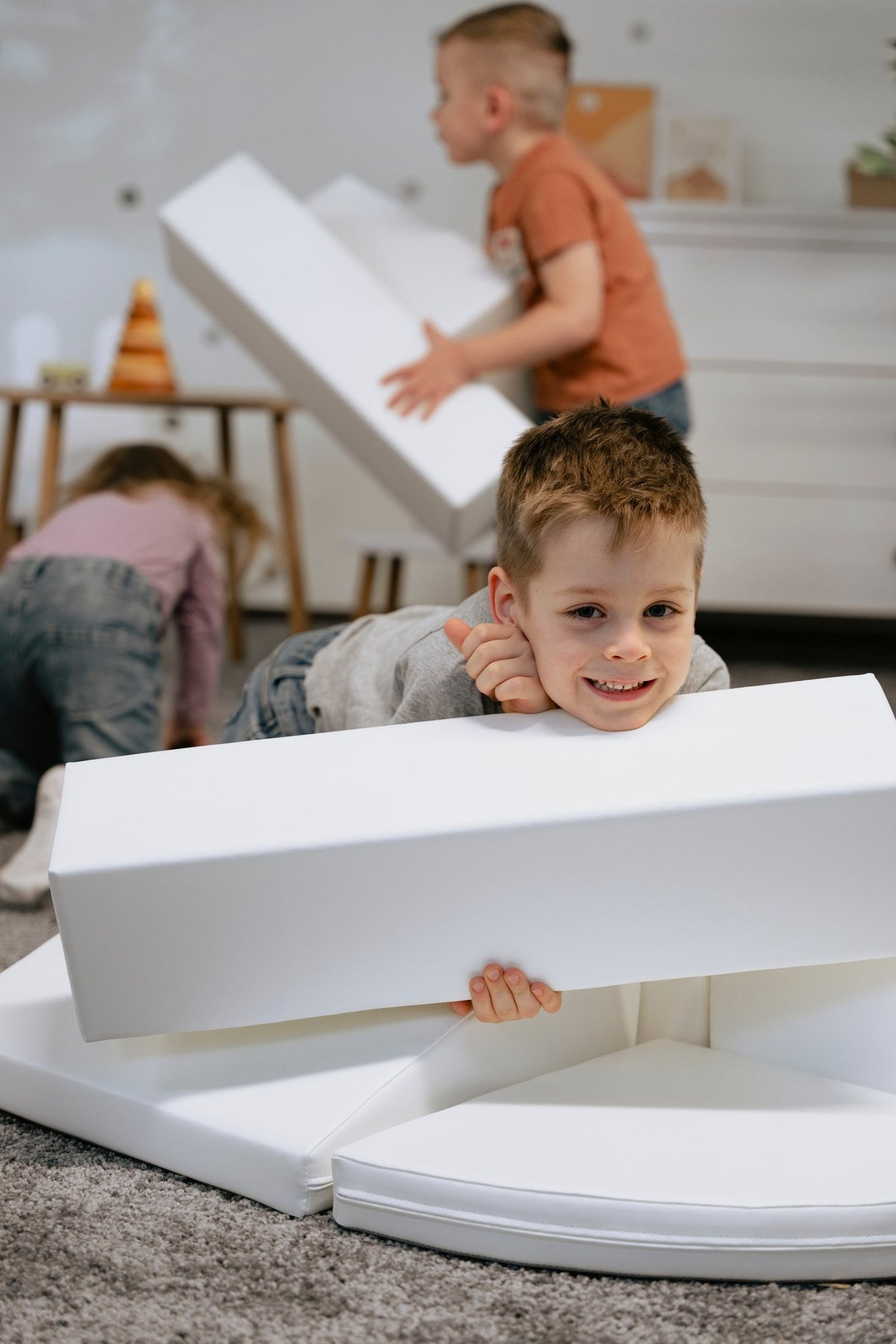 1. Child smiling while playing with white foam blocks in a playroom, part of IGLU Adventurer set
