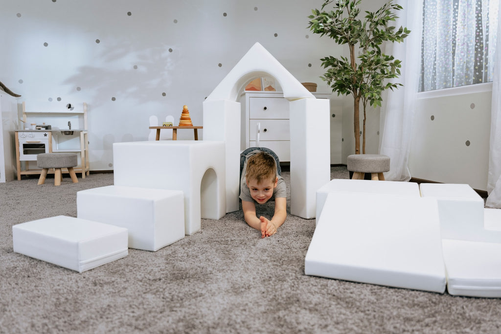 1. Child crawling through white foam block tunnel in a playroom setting with IGLU Adventurer playset