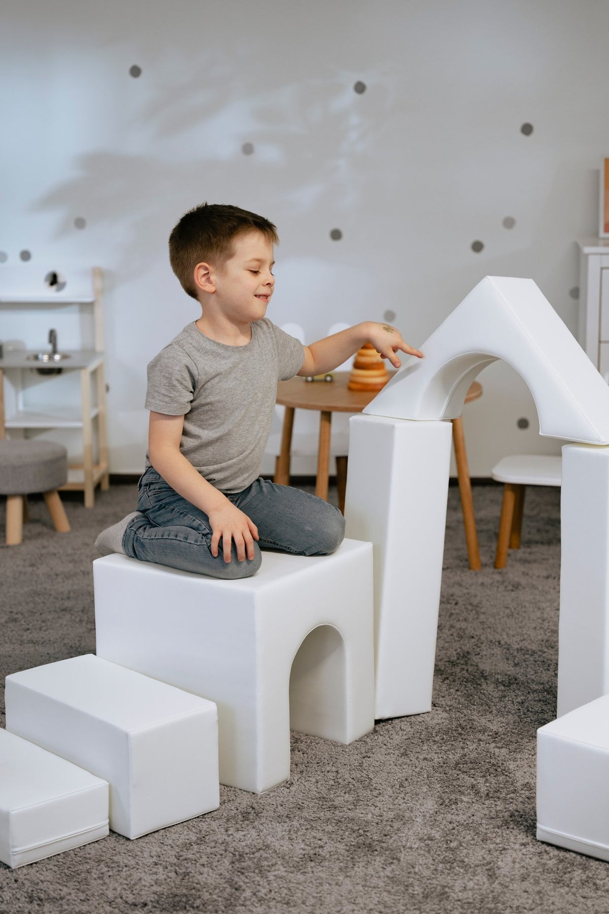 1. Child sitting on white foam block structure in a playroom, part of IGLU Adventurer set