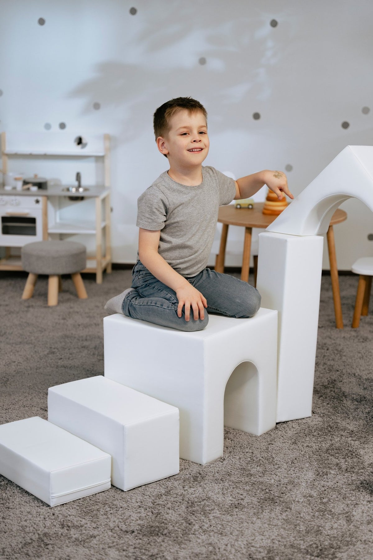 1. Child sitting on white foam block structure in a playroom, part of IGLU Adventurer set