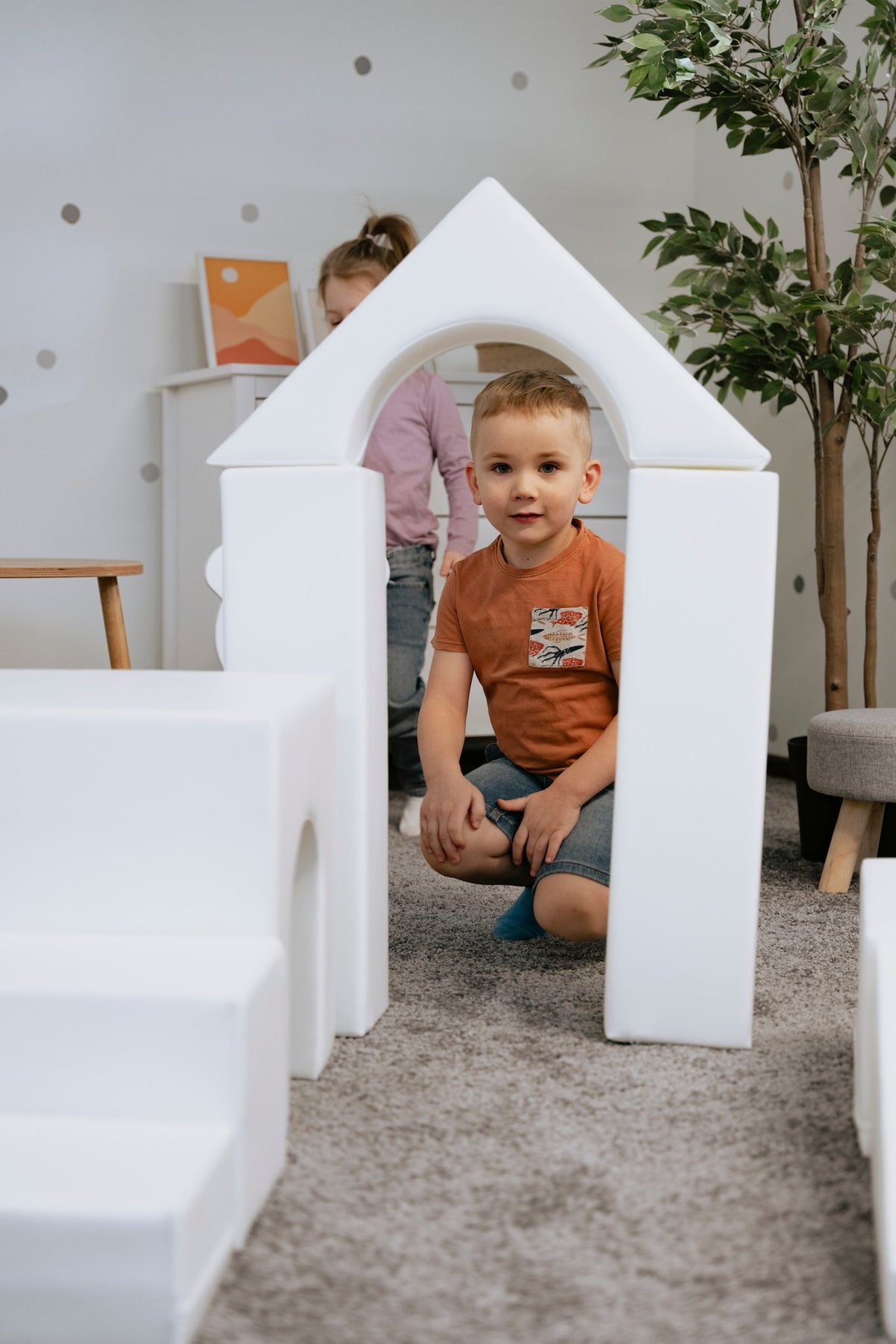 1. Child sitting inside a white foam block archway in a playroom, part of IGLU Adventurer set