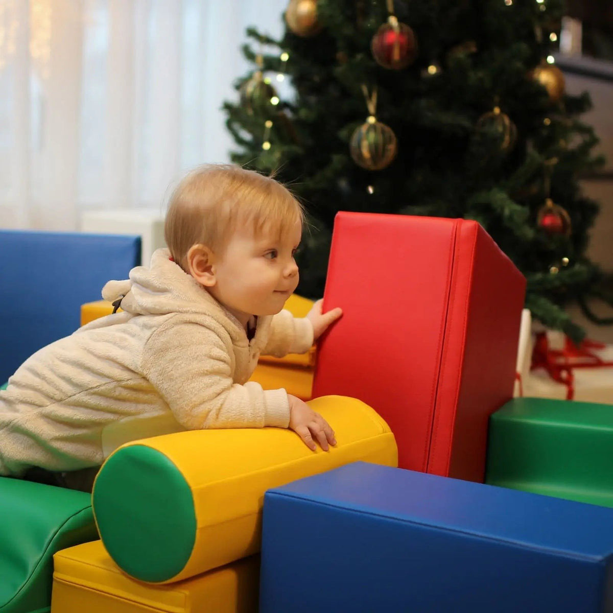 1. Baby climbing on multicolor foam blocks near Christmas tree