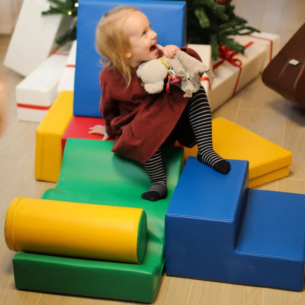 1. Girl sitting on multicolor foam blocks holding a toy near Christmas tree